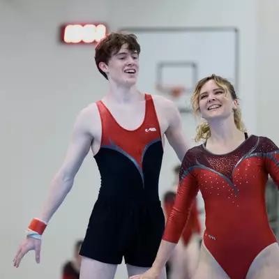 Two smiling gymnasts in red leotards, a young man and a woman, standing together after completing their performance