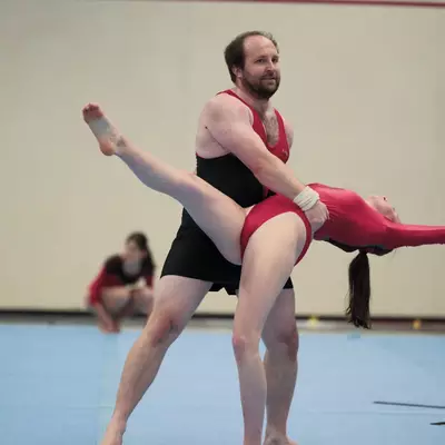 Acrobatic pairs routine: a male gymnast holds a female gymnast horizontally at waist height in an arabesque lift